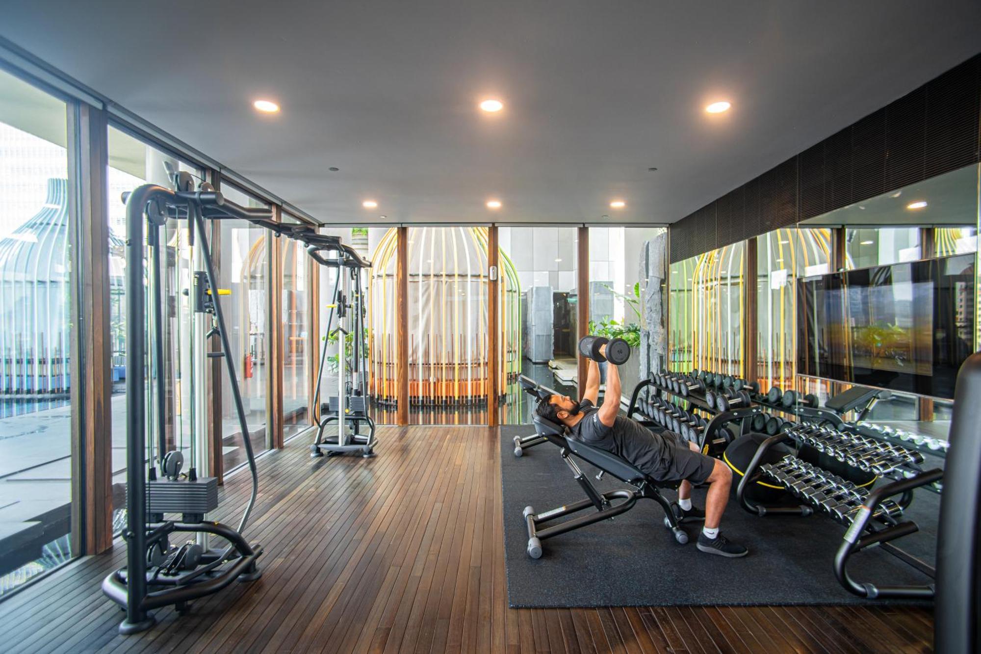 新加坡皮克林宾乐雅臻选酒店 外观 照片 The photo shows a modern gym or fitness area that features various exercise equipment. In the foreground, a person is lying on a bench and performing a dumbbell press with weights. Surrounding them are several dumbbells neatly arranged on a rack. The