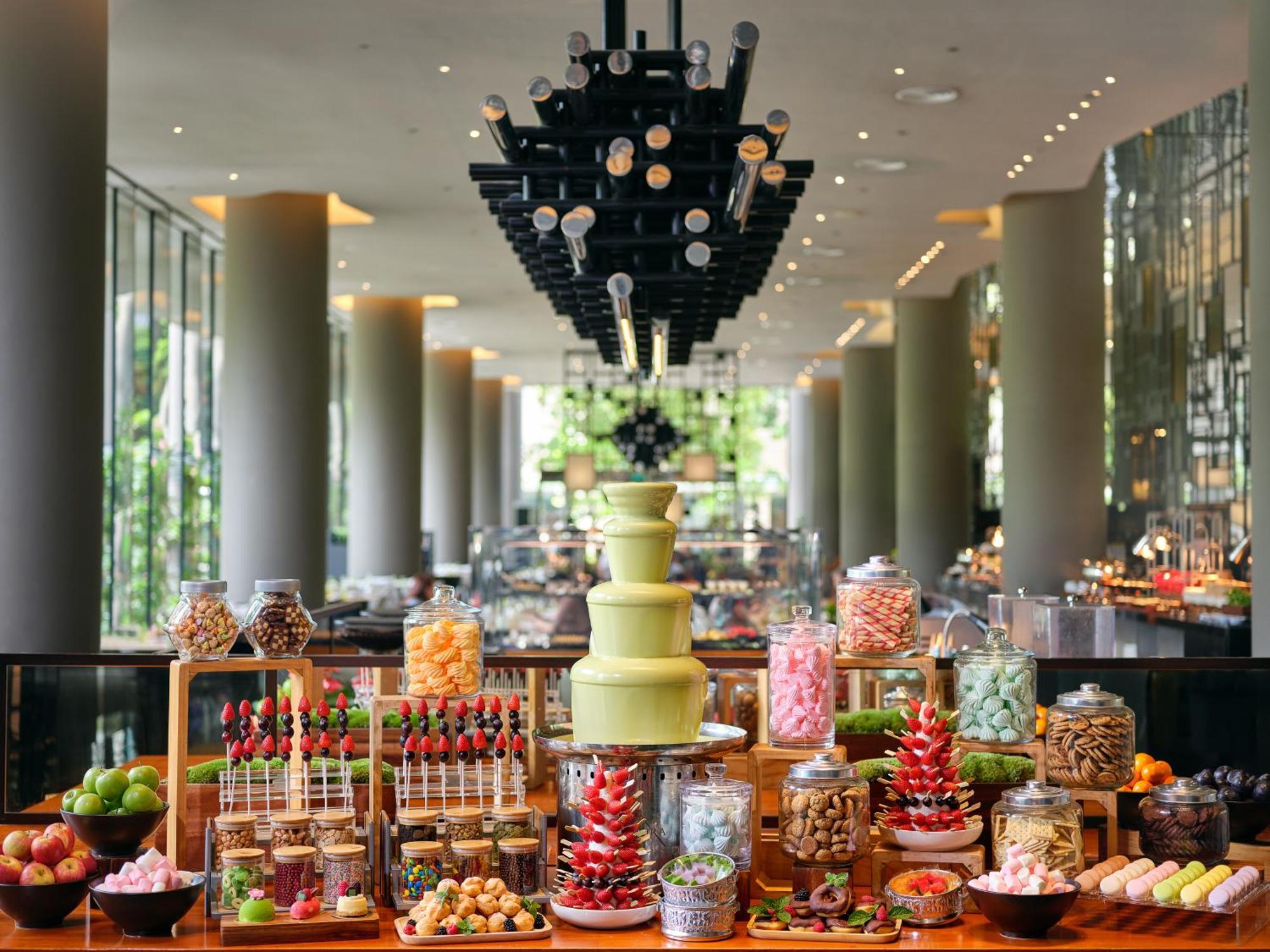 新加坡皮克林宾乐雅臻选酒店 外观 照片 The photo showcases an elegant dessert buffet set up in a modern space. In the foreground, there are various colorful treats displayed, including a tiered cake stand holding an array of sweets. The arrangement features jars filled with candies, choco