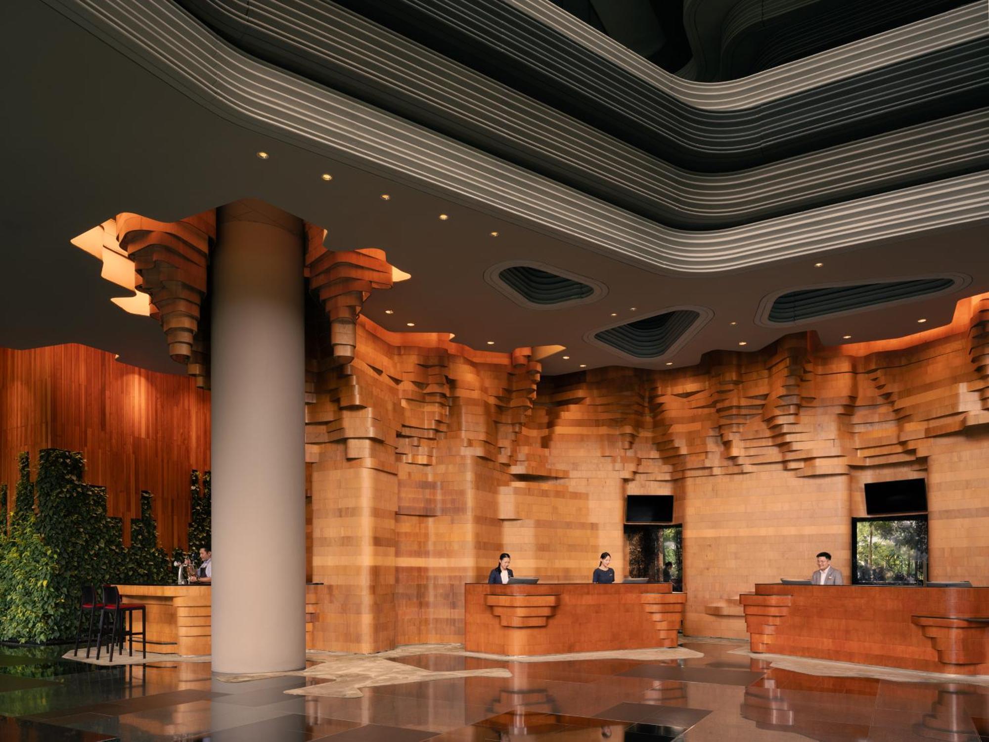 新加坡皮克林宾乐雅臻选酒店 外观 照片 The image shows a modern hotel or building lobby with a sophisticated design. The interior features richly textured wooden walls that resemble natural formations, creating a warm and inviting atmosphere. The reception area has several service counter