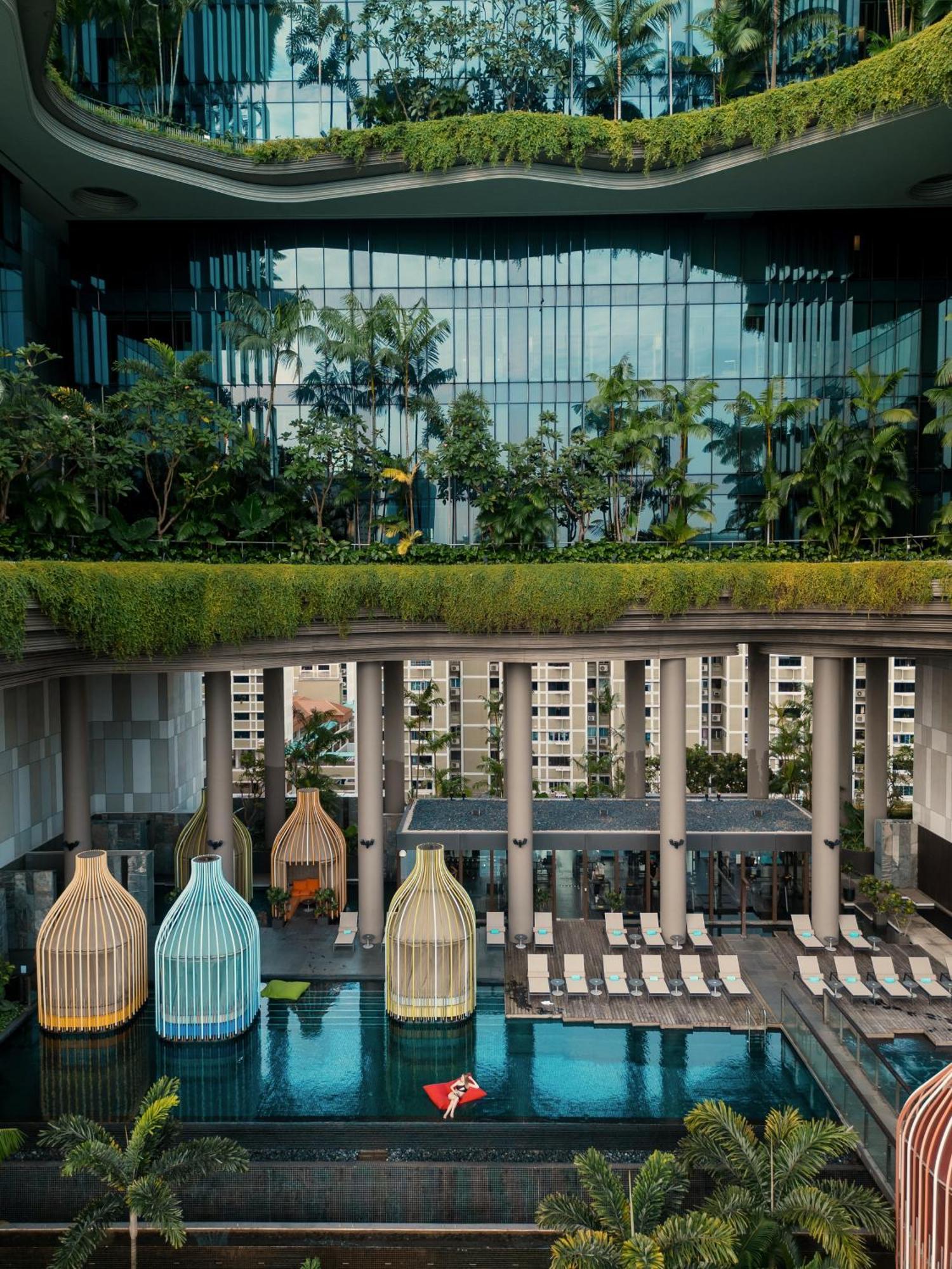 新加坡皮克林宾乐雅臻选酒店 外观 照片 The photo depicts a modern architectural design featuring a multi-level space. In the foreground, there are colorful structures resembling birdcages, which could be seating areas or decorative elements. Beyond them, there is a pool area lined with su