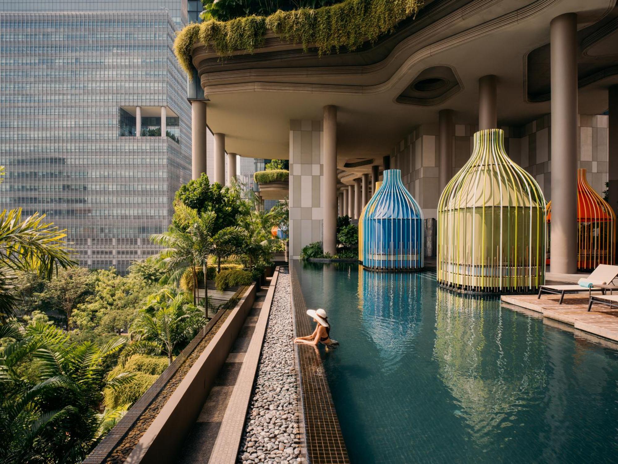 新加坡皮克林宾乐雅臻选酒店 外观 照片 The photo depicts a beautiful, modern swimming pool area surrounded by lush greenery. There are distinctive, colorful structures resembling large birdcages in blue and green, which add an artistic touch to the scene. A person is seen lounging peacefu